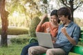 Couple young asian man and woman working with laptop and enjoying cheerful his online winner success  on a bench in the park Royalty Free Stock Photo