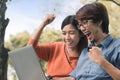 Couple young asian man and woman working with laptop and enjoying cheerful his online winner success  on a bench in the park Royalty Free Stock Photo