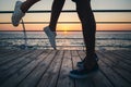 Couple of young hipster lovers kissing, close up on legs and sneakers at the beach at sunrise sky at wooden deck summer time Royalty Free Stock Photo