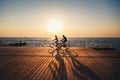 Couple of young hipsters cycling together at the beach at sunrise sky at wooden deck summer time Royalty Free Stock Photo
