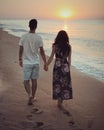 Couple of young man and woman walking on the beach coast near the sea and watching on the sunrise