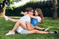 Couple of young people on grass in summer park. Pretty girl with long curly hair in shorts is sitting on handsome guy in Royalty Free Stock Photo