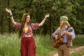 Couple of young people in hippie style. A girl is dancing, a guy is playing a guitar on a country road Royalty Free Stock Photo