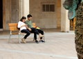 Couple of young people are sitting on a bench are attentively watching and checking their mobile phone