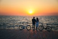 Couple of young travellers hugging at the beach and watching the sunrise at wooden deck with two bicycles near, summer time Royalty Free Stock Photo