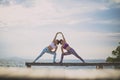 Couples of woman playing yoga pose on beach pier with moring sun light Royalty Free Stock Photo