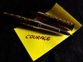 courage word written on yellow color paperslip with pen on dark background Royalty Free Stock Photo