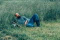 Courageous man with beard resting in the grass in field. Pensive gaze directed to sky. Next to him is ax and warrior helmet