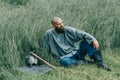 Courageous man with beard resting in the grass in field. Pensive gaze directed to sky. Next to him is ax and warrior helmet