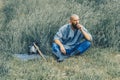 Courageous man with beard resting in the grass in field. Pensive gaze. Next to him is ax and warrior`s helmet