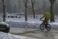 A courier with an advertising box rides a bicycle after a winter snowfall in a big city.