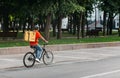 Courier bicycle delivery service. Man with large yellow backpack ride along road in park
