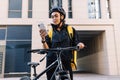 Courier with bike delivering food. Young courier checking delivery address on smartphone
