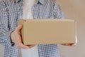 Courier in a check shirt holds out a sealed cardboard box. Delivery of online orders