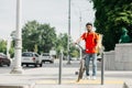 Courier and city traffic. Guy with beard in protective helmet with yellow backpack and bicycle, stands at crossroads Royalty Free Stock Photo