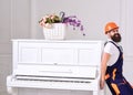 Courier delivers furniture, move out, relocation. Man with beard worker in helmet and overalls pushes, put efforts to Royalty Free Stock Photo