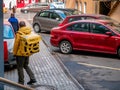 Courier of food delivery service in a branded uniform with a yellow Yandex-Eda backpack next to parked cars. Thermal bag with symb