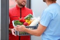 Courier giving plastic crate with products to customer at home, closeup. Food delivery