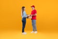 Courier Guy Giving Cardboard Parcel Boxes To Lady, Yellow Background Royalty Free Stock Photo