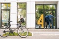 Courier male with large thermo backpack delivered an online order on the bicycle, calling on intercom on house wall. Royalty Free Stock Photo