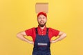 Courier man wearing blue uniform standing with hands on hips and holding cardboard box on his head. Royalty Free Stock Photo