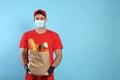 Courier in medical mask holding paper bag with food on light blue background, space for text. Delivery service during quarantine Royalty Free Stock Photo