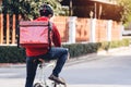 Courier in red uniform with a delivery box on back riding a bicycle and looking on the cellphone to check the address to deliver