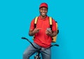 Black delivery man riding bicycle, using smartphone