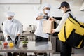 Courier waiting for an order for delivery in the kitchen with chefs preparing takeaway food