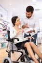 Courteous man helping a woman in a wheelchair to choose the right medicine in pharmacy