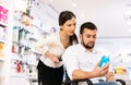Courteous woman helping man in a wheelchair to choose the right medicine in pharmacy