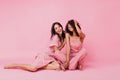 Cousins in chic summer cotton dresses are chatting nicely. Young women posing on light pink backgro Royalty Free Stock Photo