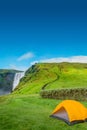 Cover page camping site with orange tent, and tourists in front of famous Skogafoss waterfall, while hiking in Iceland, summer, Royalty Free Stock Photo