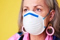 Cover up and help reduce the spread. a quirky senior woman wearing a N95 face mask against a yellow background.