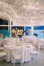 Covered festive tables with bouquets of flowers on stands stand on the terrace by the sea