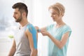 Physiotherapist covering selected fragments of young man`s body with special structure patches during kinesiotaping therapy Royalty Free Stock Photo