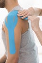 Physiotherapist covering selected fragments of young man`s body with special structure patches during kinesiotaping therapy Royalty Free Stock Photo