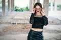 A coveted woman or girl stands in the middle of an abandoned building in a leather skirt top and sunglasses, brunette