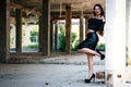 A coveted woman or girl stands in the middle of an abandoned building in a leather skirt top and sunglasses, brunette