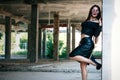 A coveted woman or girl stands in the middle of an abandoned building in a leather skirt top and sunglasses, brunette