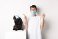 Covid-19, animals and quarantine concept. Young man and black dog wearing medical masks, pug looking at upper left Royalty Free Stock Photo