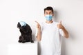 Covid-19, animals and quarantine concept. Young man and black dog wearing medical masks, pug looking at upper left Royalty Free Stock Photo