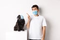 Covid-19, animals and quarantine concept. Young man and black dog wearing medical masks, pug and owner looking at upper Royalty Free Stock Photo