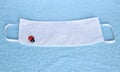 Covid-19 disposable 3-layer white filter mask with lucky charm ladybird, blue towel as a background