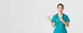 Covid-19, healthcare workers, pandemic concept. Smiling pretty asian doctor, nurse in scrubs and stethoscope, pointing Royalty Free Stock Photo