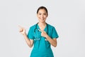 Covid-19, healthcare workers, pandemic concept. Smiling pretty asian doctor, nurse in scrubs and stethoscope, pointing Royalty Free Stock Photo