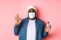 Covid-19, lifestyle and lockdown concept. Handsome african-american hipster guy in face mask and beanie, showing hand Royalty Free Stock Photo