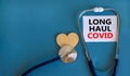 COVID-19 long-haul covid symptoms symbol. White card with words Long haul covid. Wooden heart, stethoscope, beautiful blue