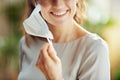 Smiling female in grey blouse taking off ffp2 mask