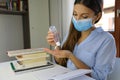 COVID-19 Pandemic Woman with Surgical Mask Studying from Home using Alcohol Gel from Dispenser against 2019-nCoV. Home